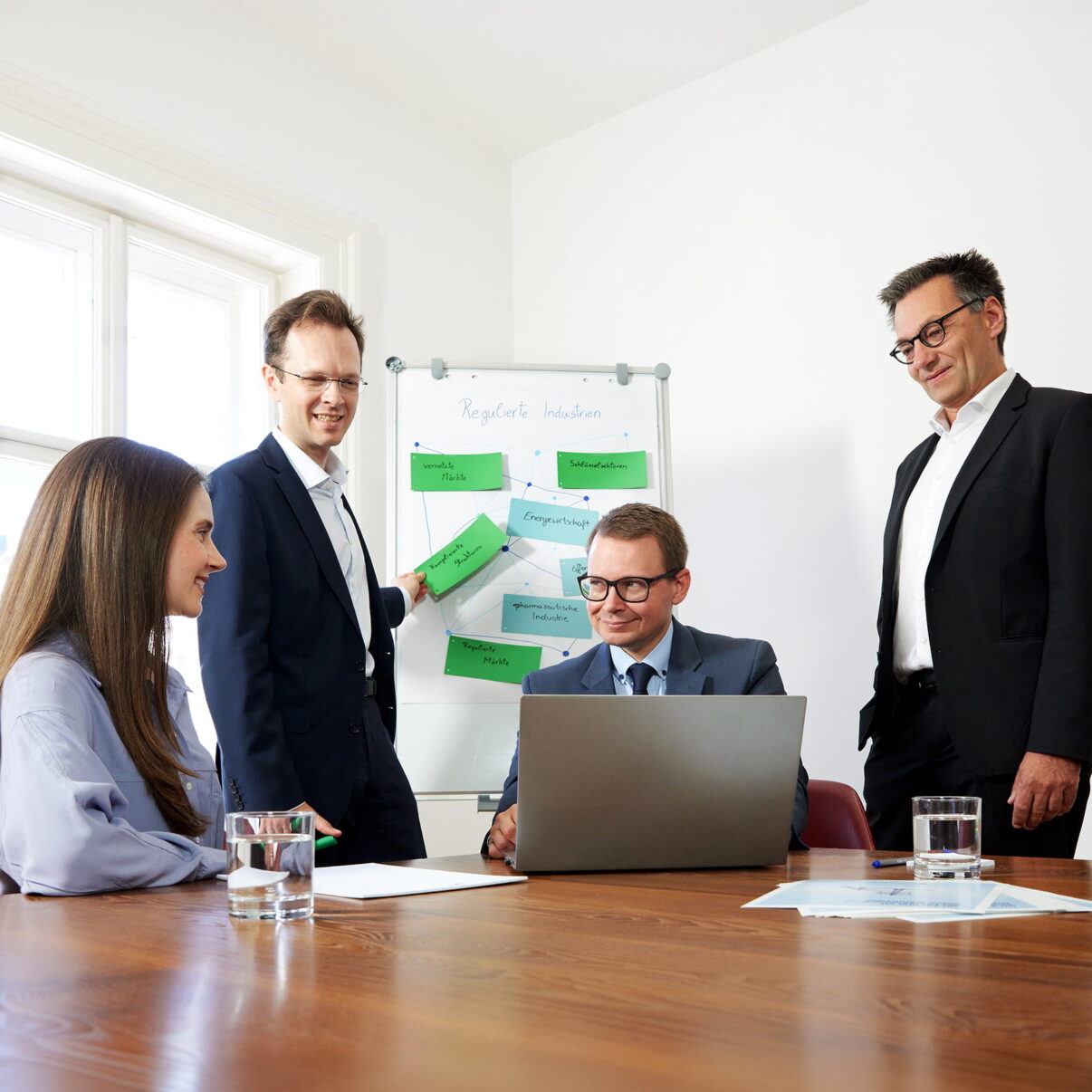 Vier Teammitglieder des Teams Regulierte Industrien bei einer Besprechung mit Laptop und Whiteboard.