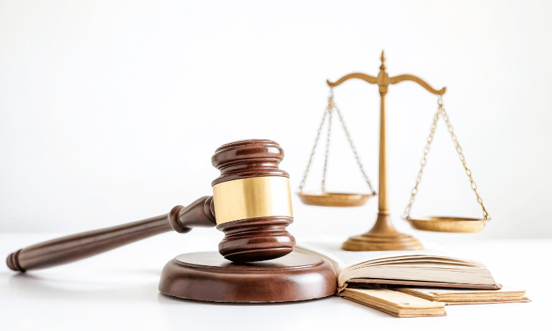 Richterhammer neben Justizwaage und Gesetzbuch, Sinnbild für rechtliche Vorgaben der Kapitalansammlungsrichtlinie
